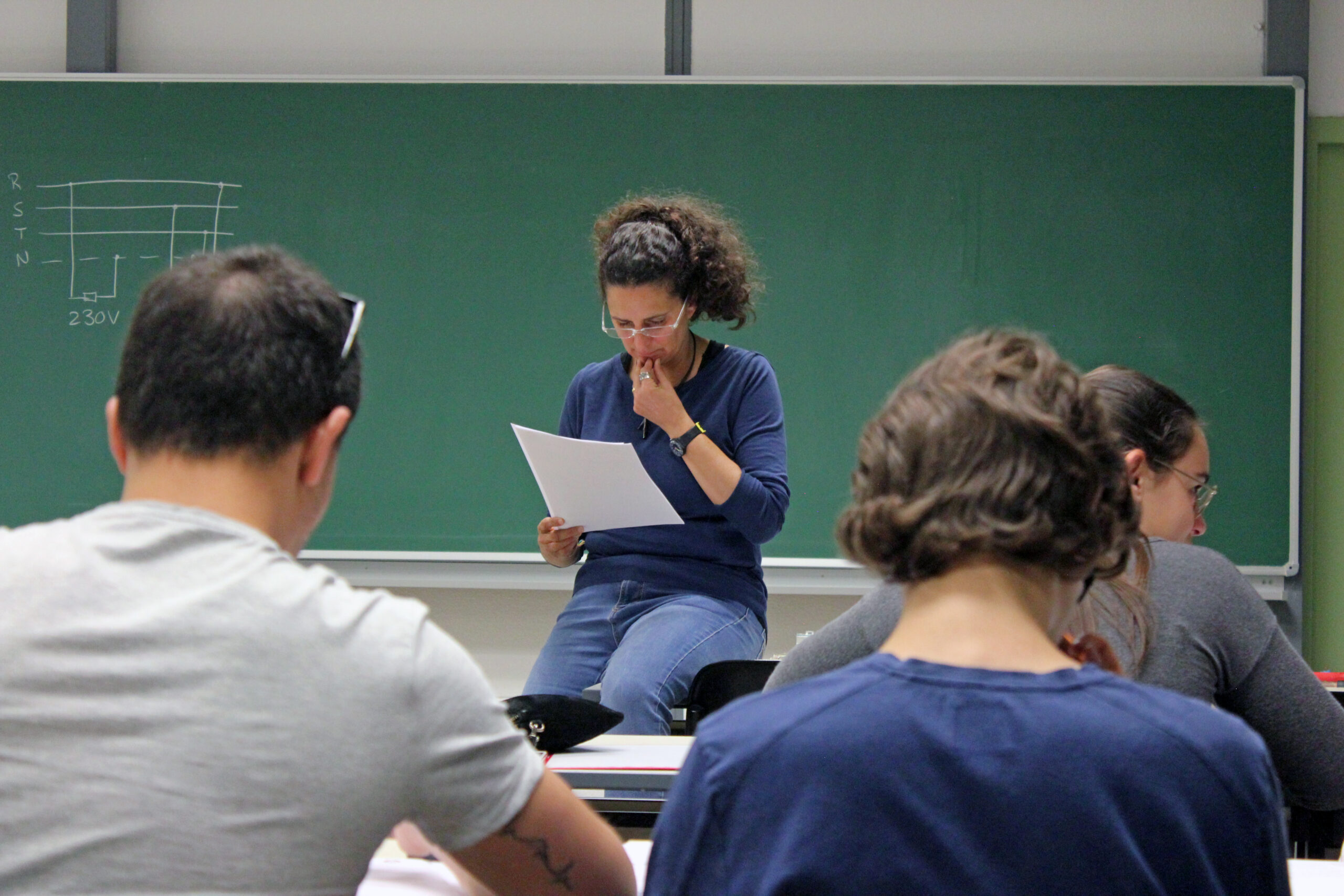 Teacher sat in a table reading a paper at class